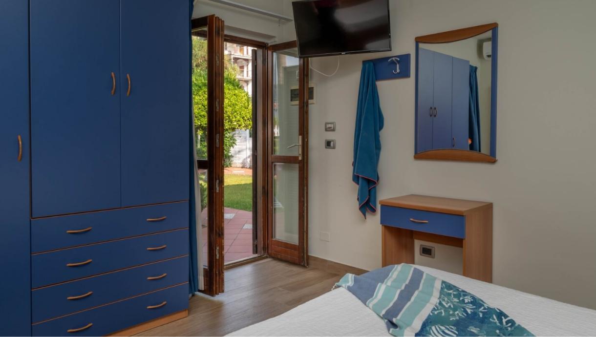 Camera da letto con mobili blu, porta finestra aperta verso il giardino.
