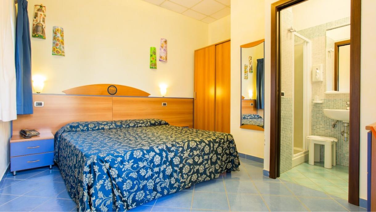 Camera d'albergo con letto matrimoniale, bagno privato e arredi in legno chiaro.