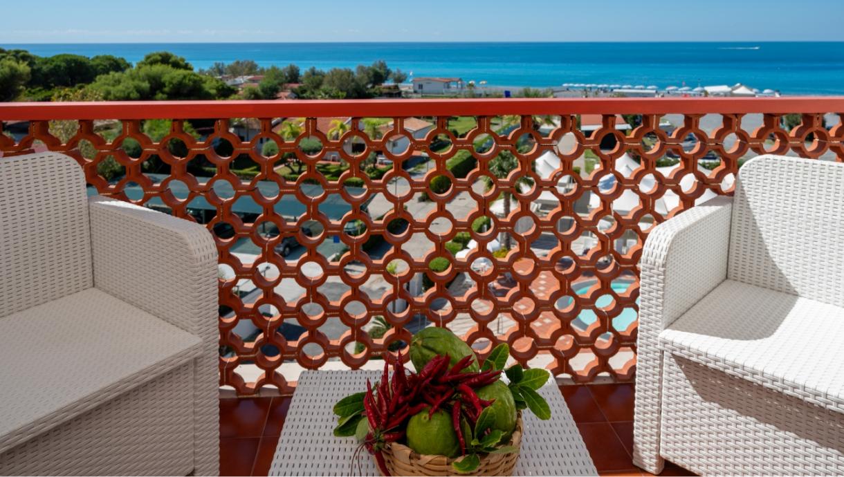 Terrazza con vista mare, sedie bianche e cesto di frutta e peperoncini.