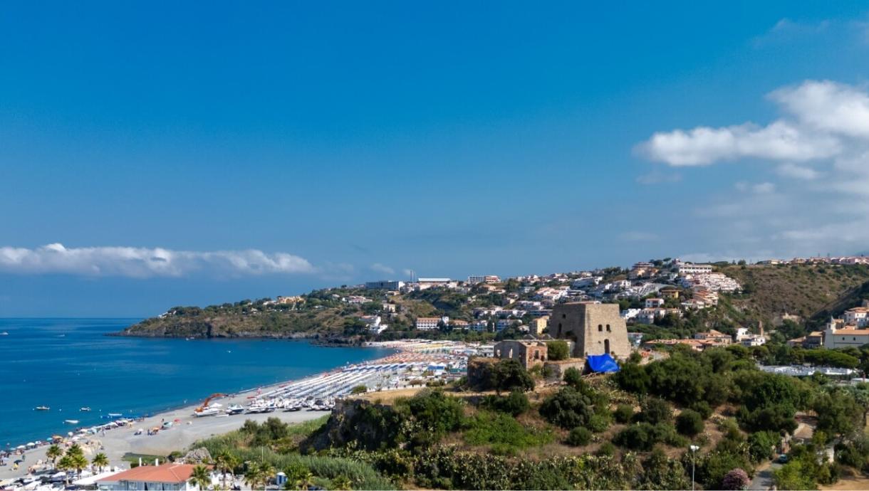Vista panoramica di una costa con spiaggia, mare e case su una collina.