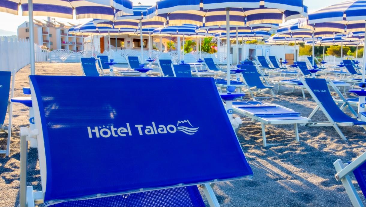 Lettini e ombrelloni blu di Hotel Talao su una spiaggia soleggiata.