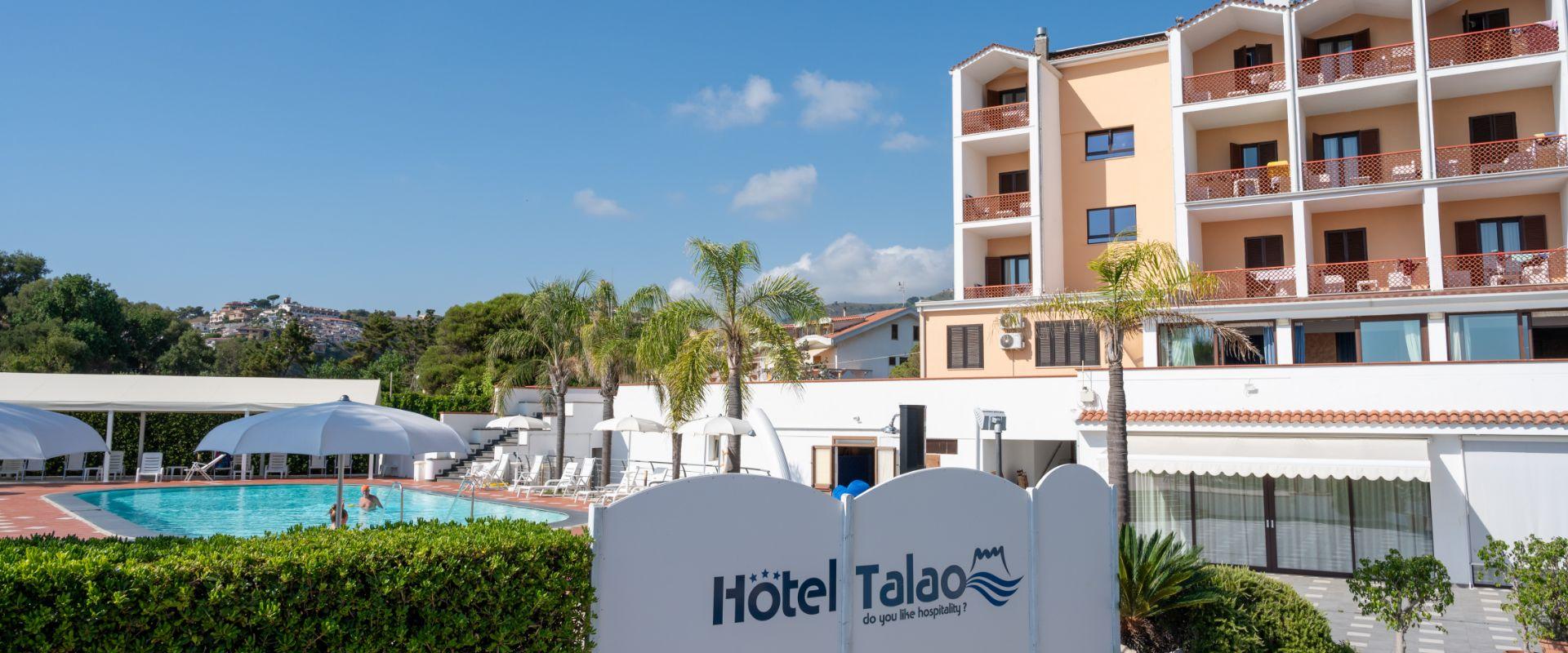 Hotel Talao con piscina, palme e vista panoramica su colline e case.