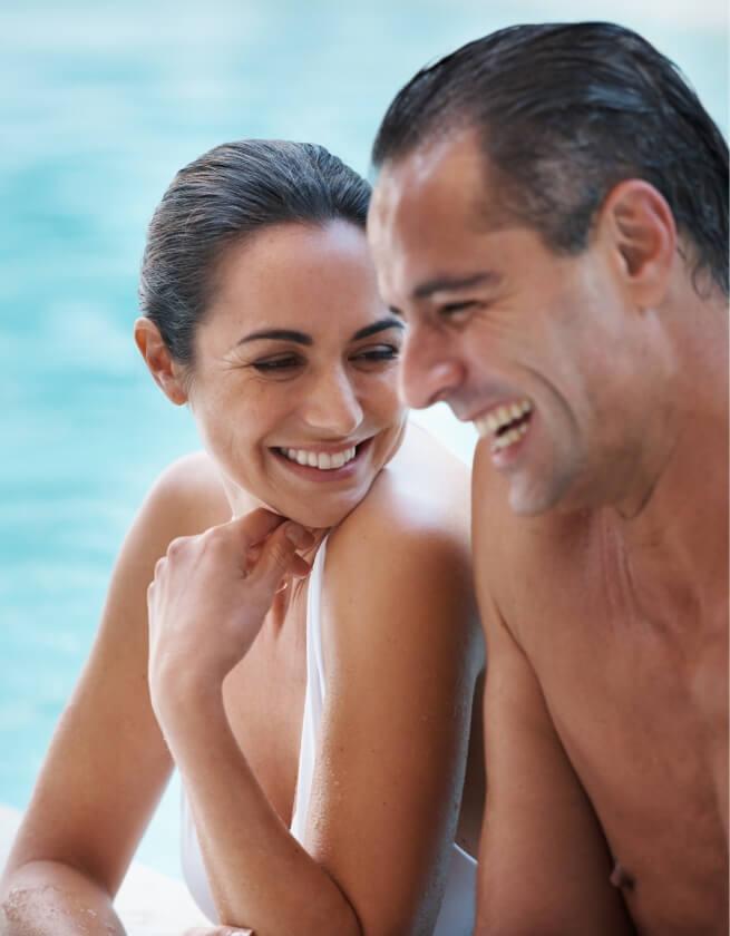Due persone sorridenti si rilassano vicino a una piscina.