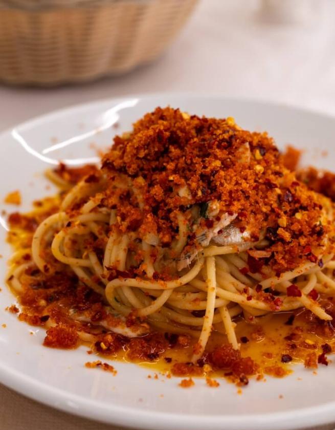 Spaghetti con pangrattato croccante e olio, serviti su un piatto bianco.