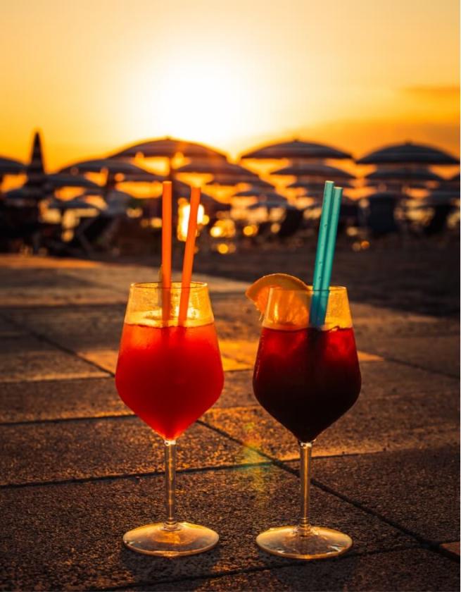 Due cocktail al tramonto su una spiaggia con ombrelloni sullo sfondo.